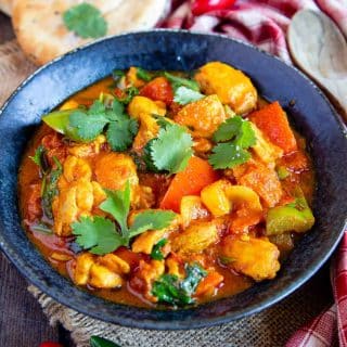 a bowl of freshly cooked chicken jalfrezi garnished with coriander leaves ready to serve with mini naan bread