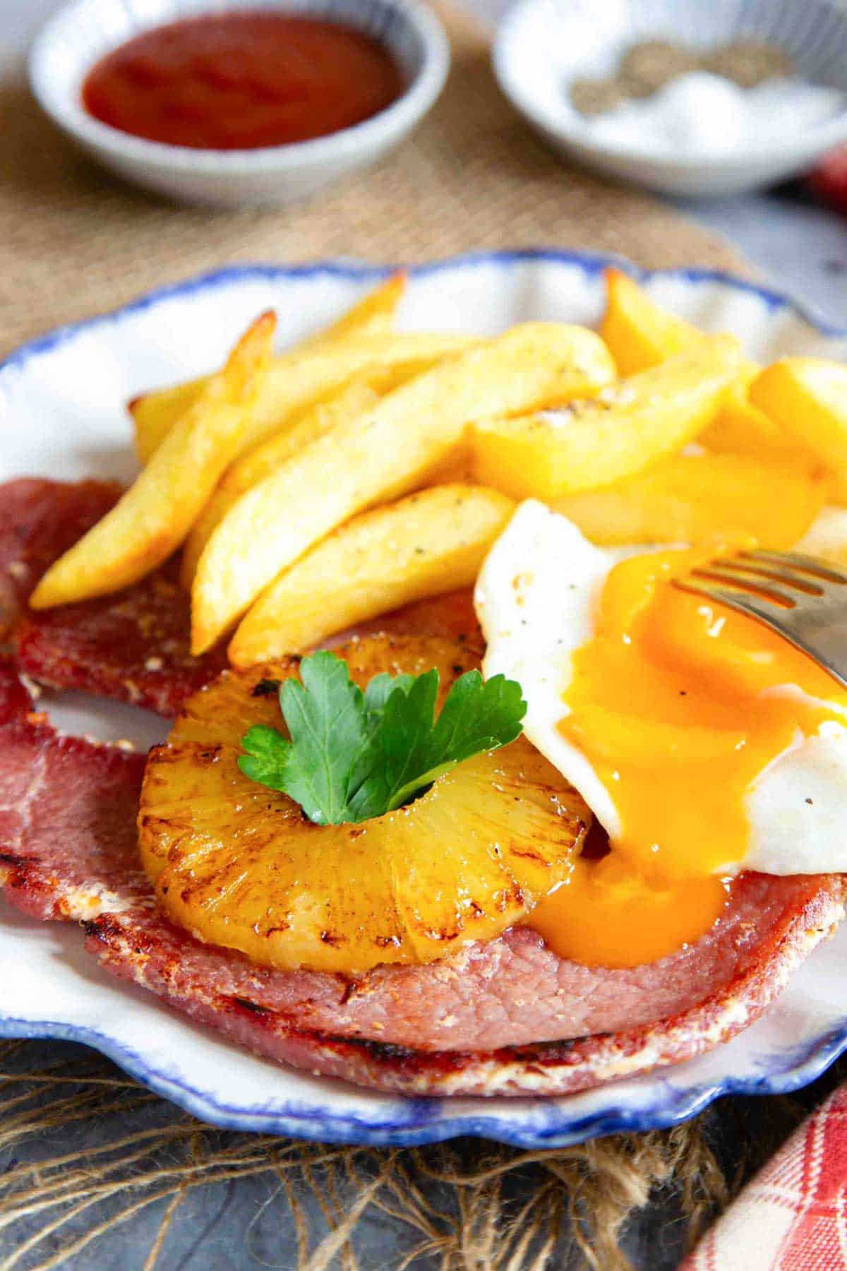 a plate of gammon, egg with runny yolk and chips with a caramelised pineapple ring served and ready to enjoy