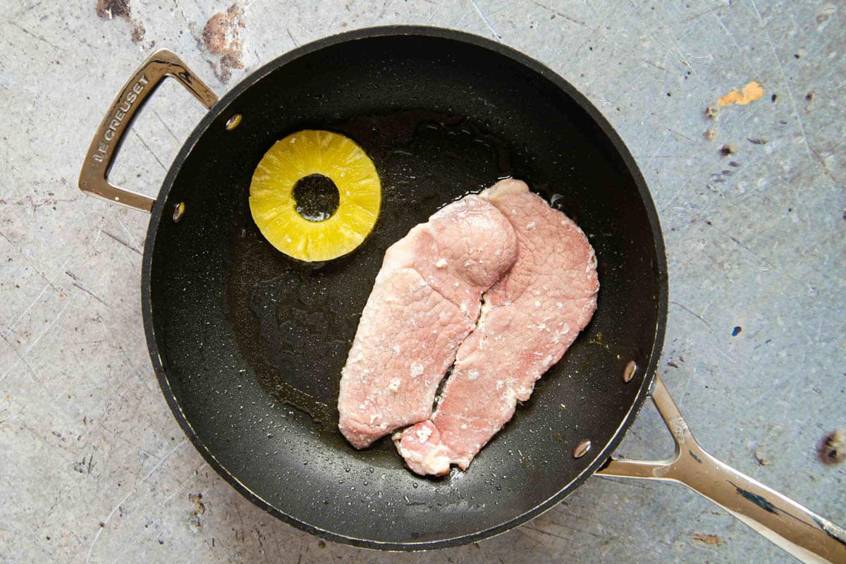 the half cooked steak has been flipped over and a pineapple ring added