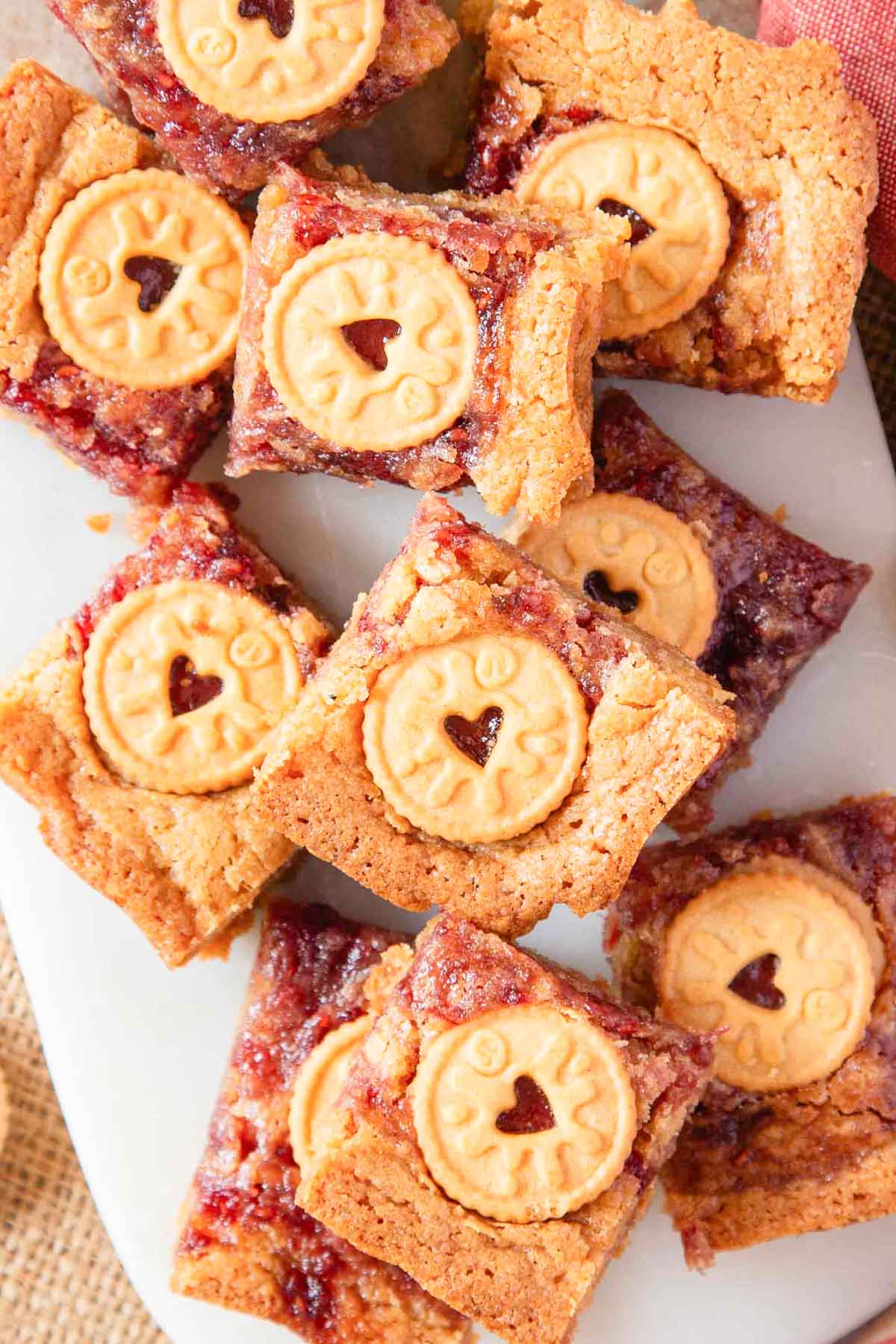 a pile of blondies swirled with jam and each topped with a mini jammie dodger biscuit