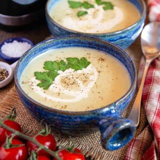 Two bowls of leek and potato soup garnished with cream and parsley