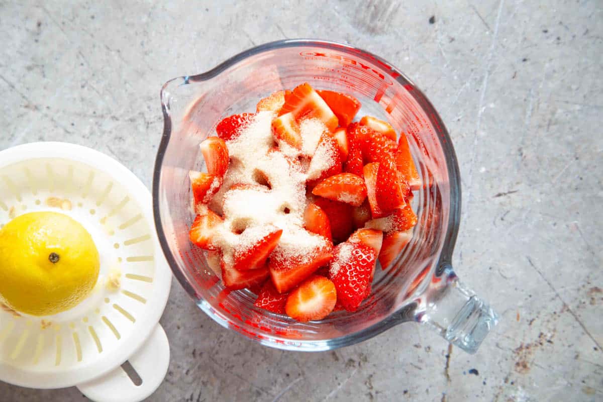 strawberries have been placed in a jug and topped with sugar and freshly squeezed lemon juice