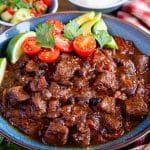a close up of a bowl of chilli con carne garnished with tomato, lime and avocado