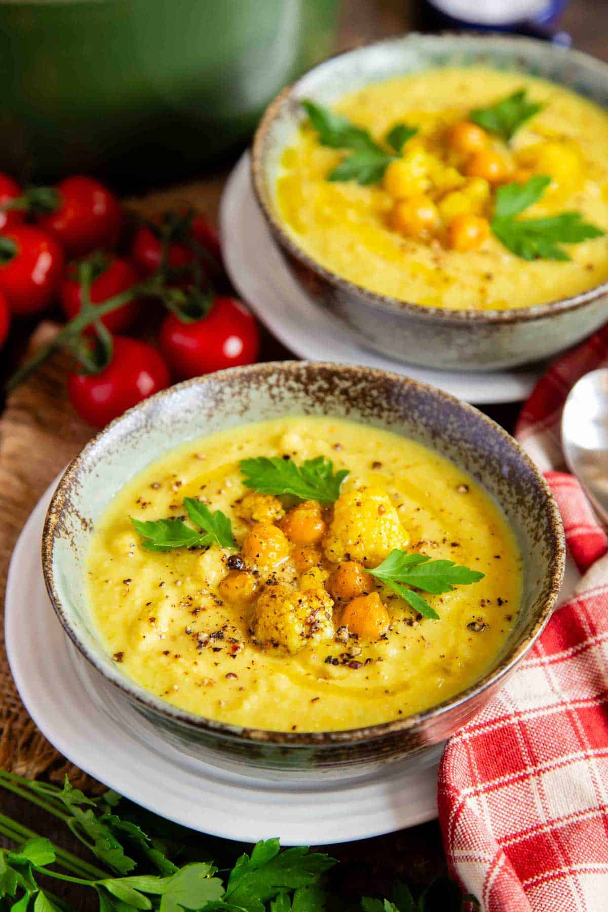 two bowls of golden soup garnished with chickpeas, cauliflower and fresh parsley