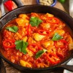 a cast iron serving bowl of chicken madras garnished with sliced red chillies and coriander