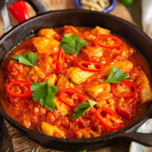 a cast iron serving bowl of chicken madras garnished with sliced red chillies and coriander