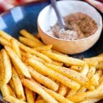 a bowl of crispy freshly cooked French fries sprinkled with fry seasoning