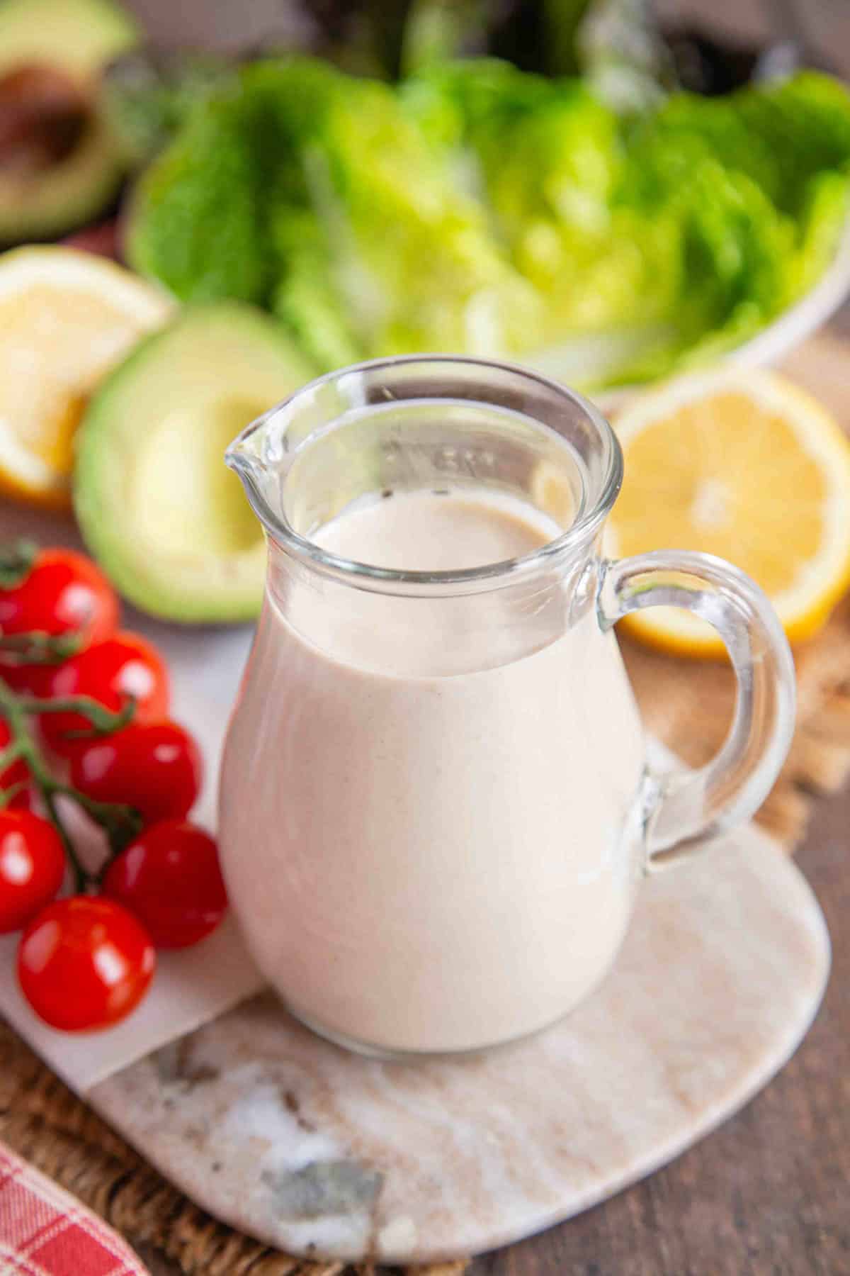 a glass jug of tahini lemon dressing with a salad behind it