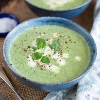 a bowl of pale green watercress soup garnished with a swirl of cream and fresh watercress