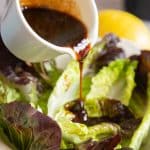 a close up of pouring the thick dark brown dressing over a bowl of green salad leaes