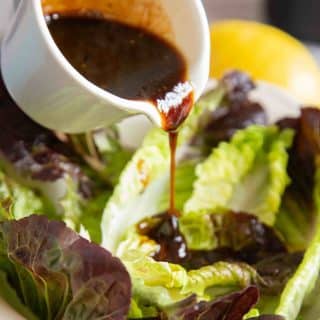 a close up of pouring the thick dark brown dressing over a bowl of green salad leaes