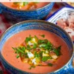 a blue soup bowl full of salmon pink salmorejo garnished with chopped hard boiled egg ham parsley and olive oil