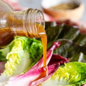 a close up of pouring the dark caramel coloured dressing onto red and green salad leaves