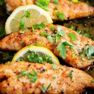 a pan of golden chicken fillets in a garlic butter sauce garnished with lemon and parsley