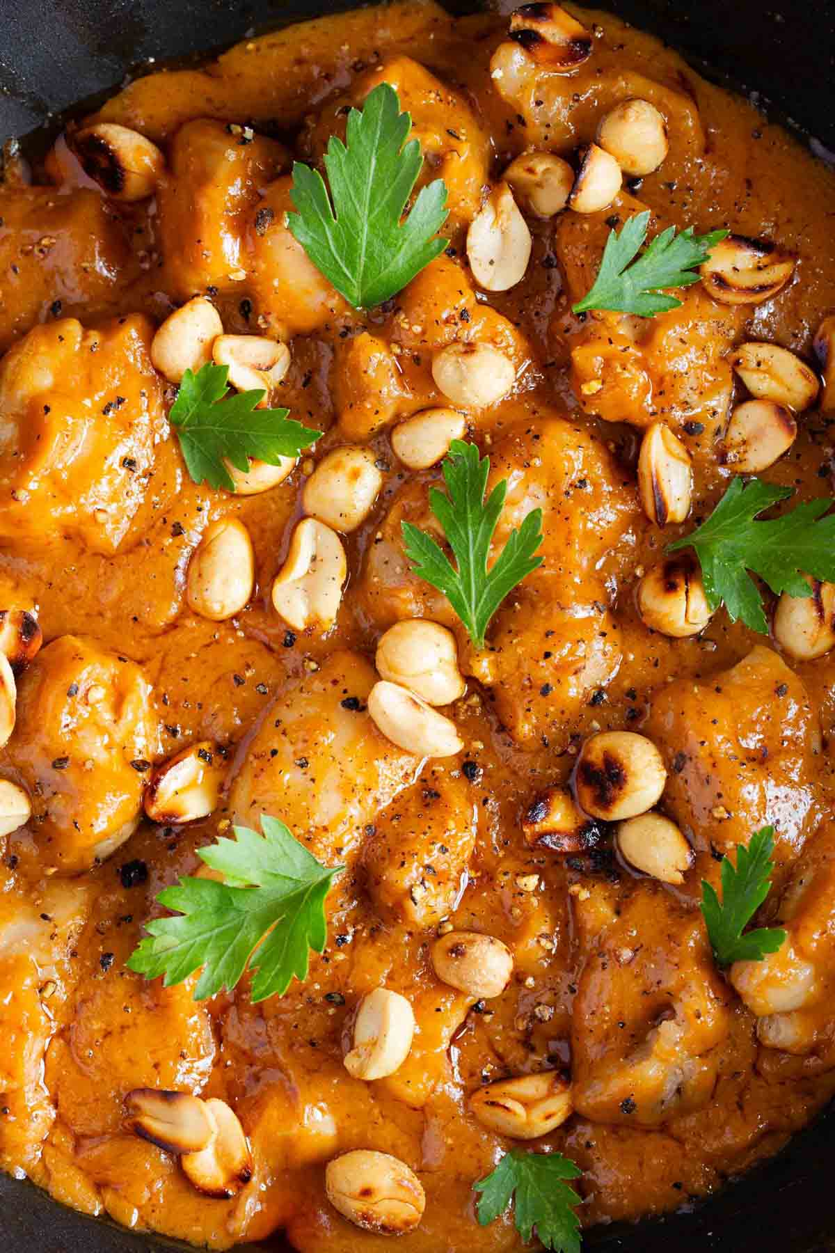 the finished dish tender chunks of chicken in a rich thick peanut butter sauce garnished with roasted peanuts and parsley