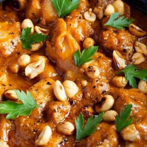 the finished dish tender chunks of chicken in a rich thick peanut butter sauce garnished with roasted peanuts and parsley