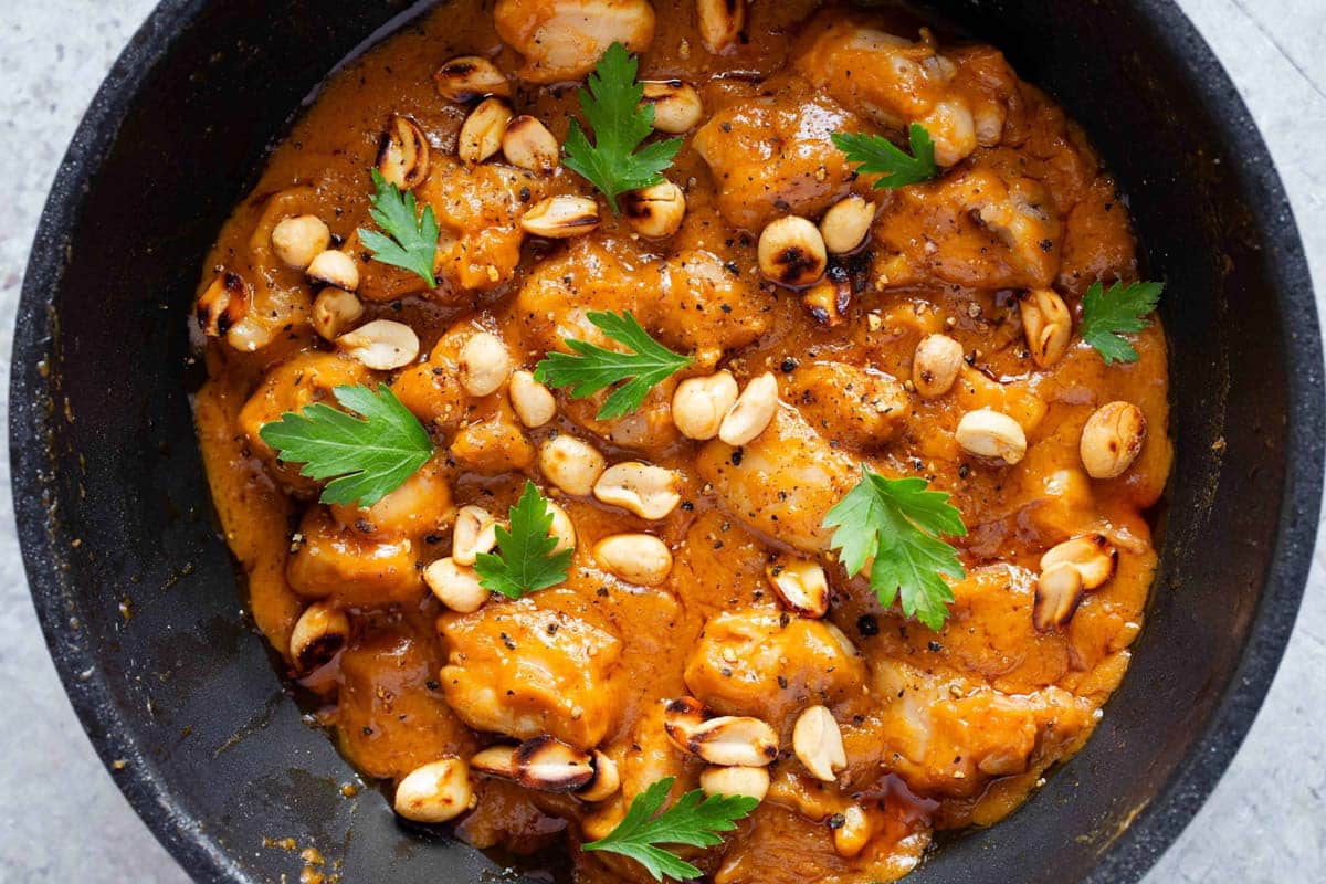 the finished dish tender chunks of chicken in a rich thick peanut butter sauce garnished with roasted peanuts and parsley