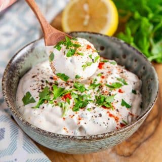 a bowl of creamy white shawarma sauce garnished with chopped parsley