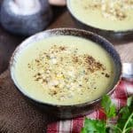 a bowl of pale green broccoli and stilton soup garnished with crumbled stilton and black pepper