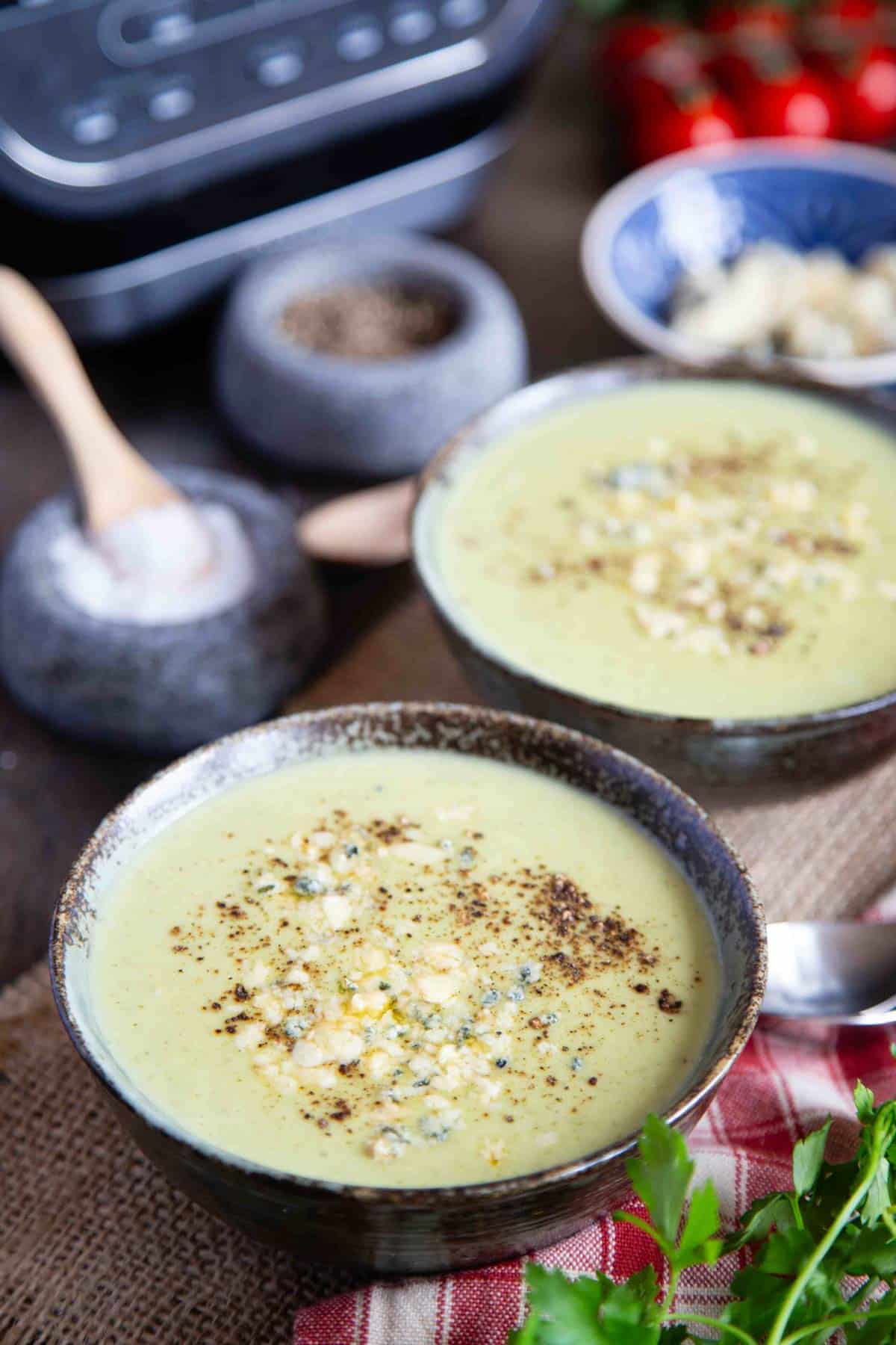 two bowls of pale green broccoli and stilton soup garnished with crumbled stilton and black pepper