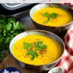 two bowls of golden butternut squash soup with the soup maker in the background