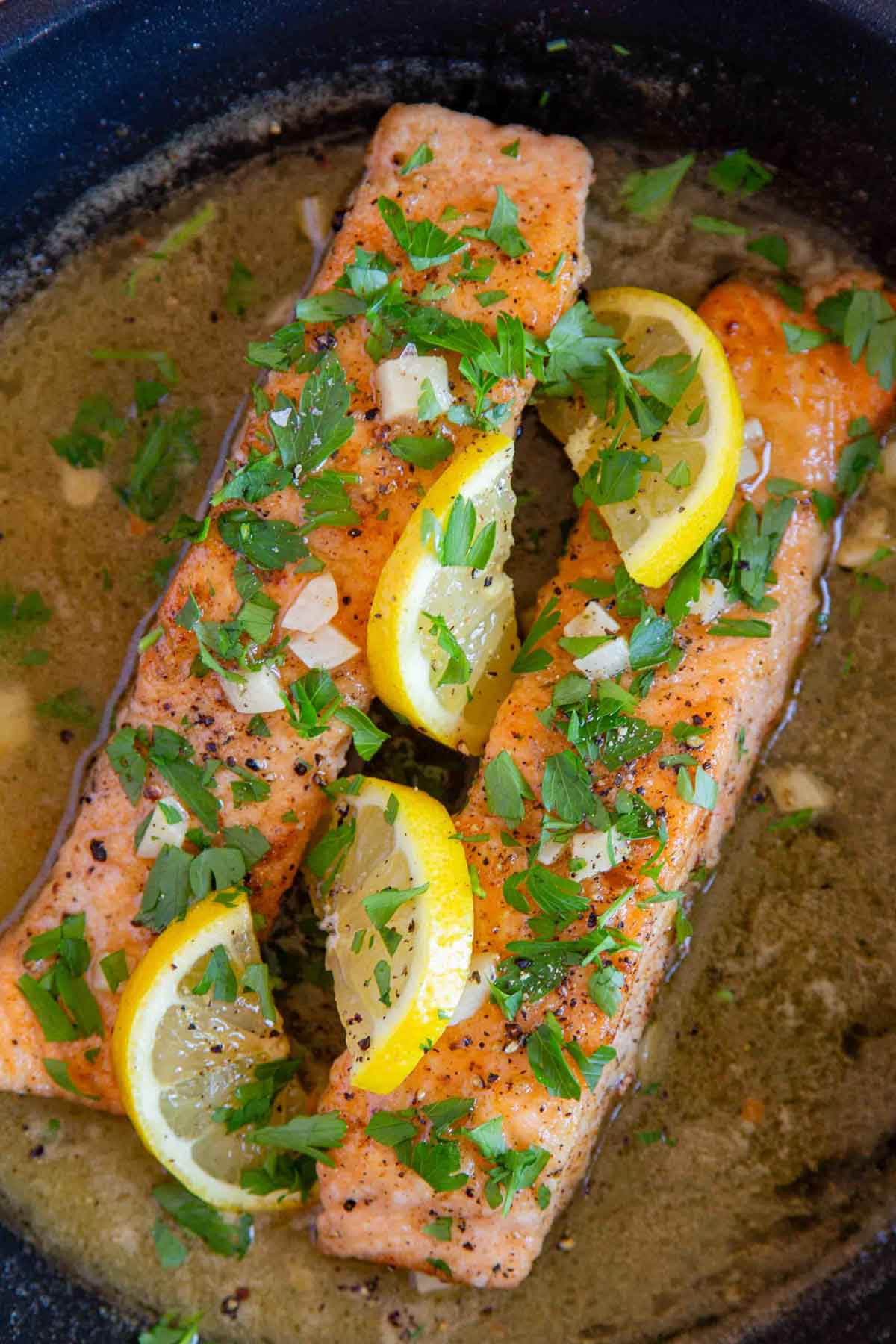 the salmon fillets in the pan with sauce spooned over and garnished with slices of lemon and chopped parsley