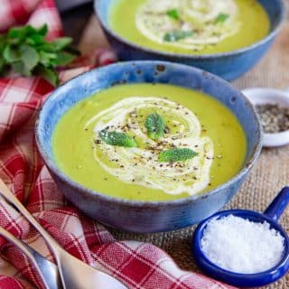 two bowls of freshly made pea soup garnished with a swirl of cream and fresh mint