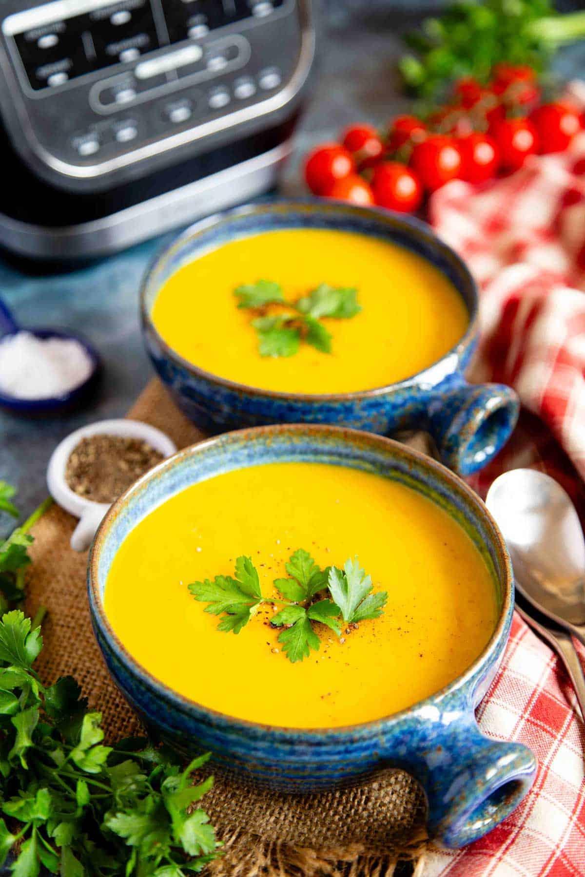 two bowls of golden mixed vegetable soup garnished with parsley