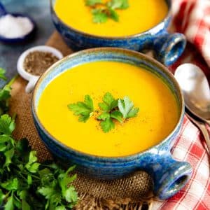 two bowls of golden mixed vegetable soup garnished with parsley