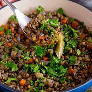A spoon of braised Puy lentils being served from a casserole dish