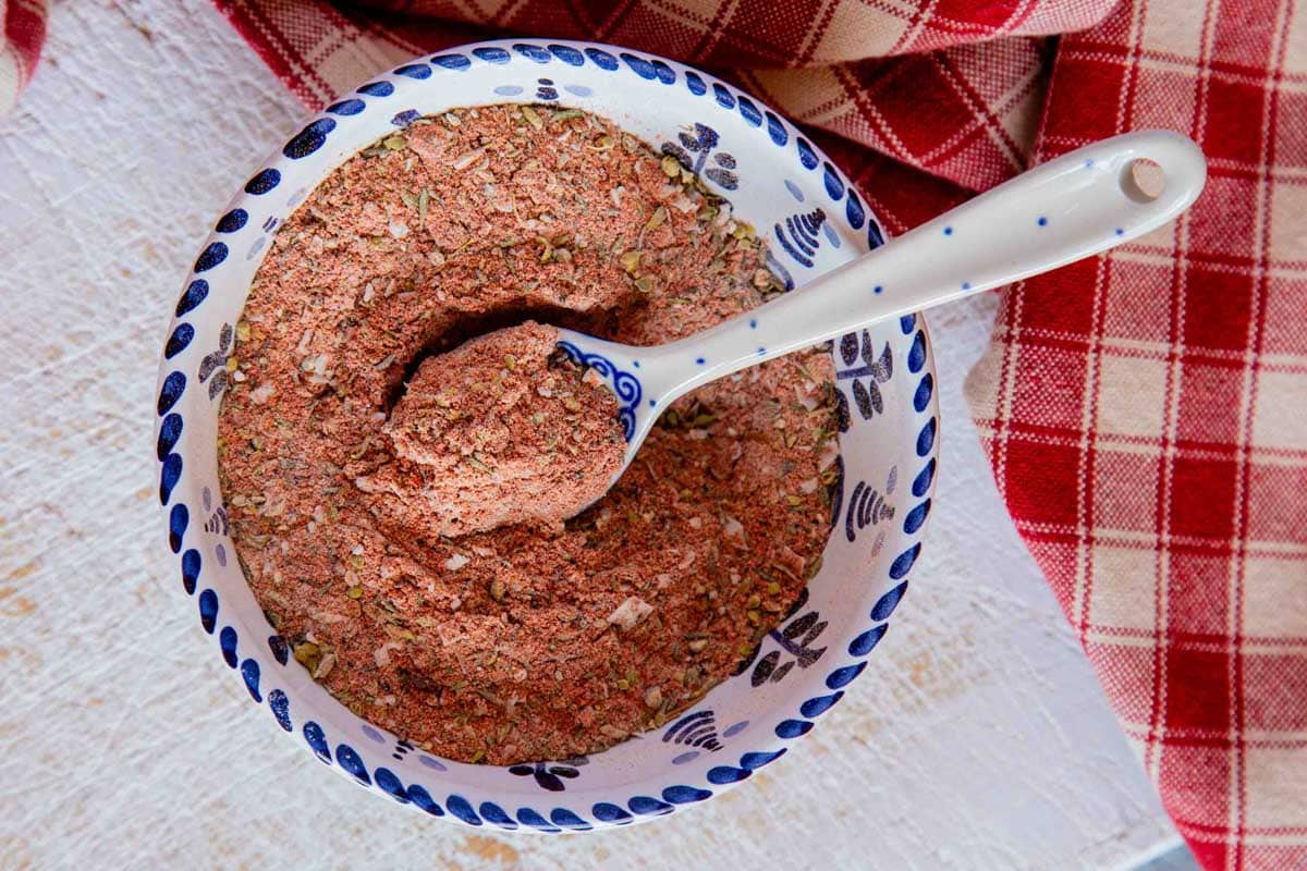 A porcelain spoon in a rustic white and blue bowl of chicken seasoning mixture.