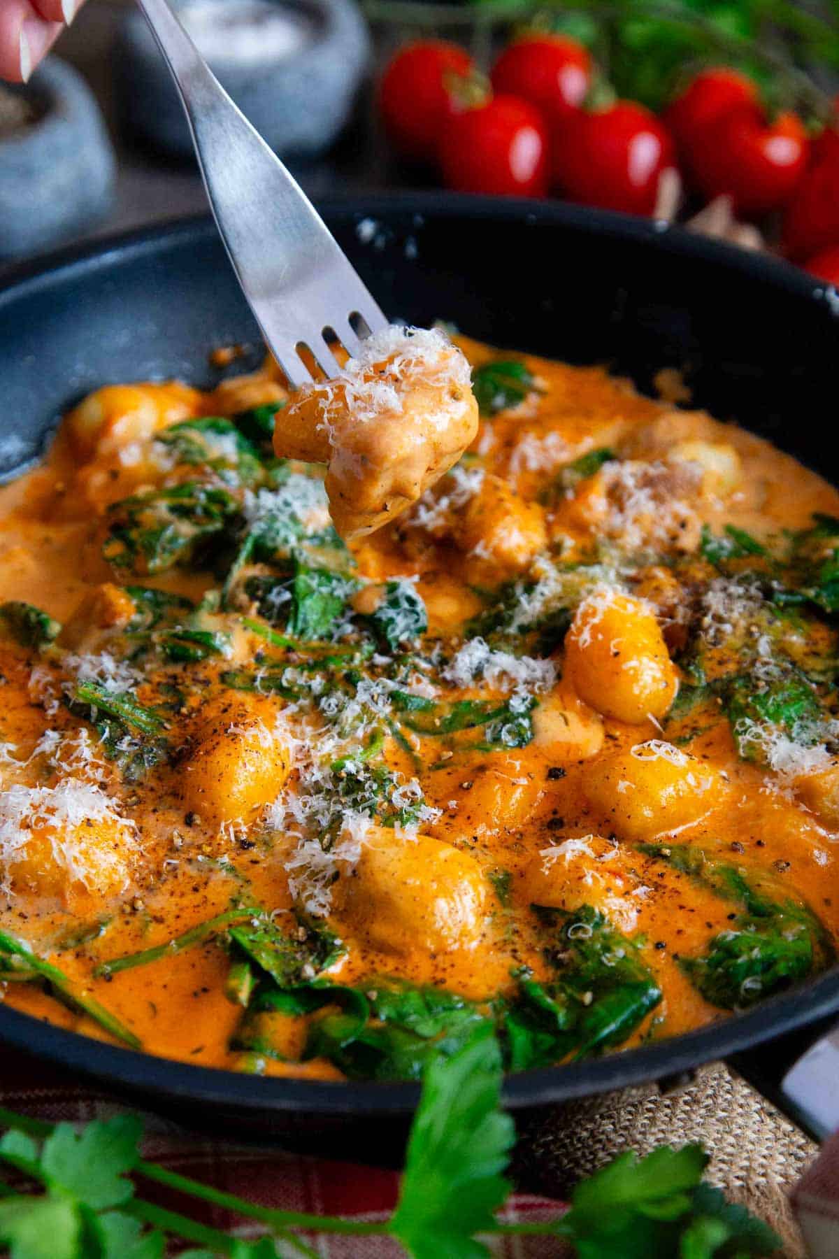 A fork is taking a gnocchi and a piece of chicken from the cooking pan