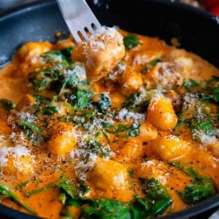 A close up of a fork loaded with creamy chicken and a piece of gnocchi above the cooked dish