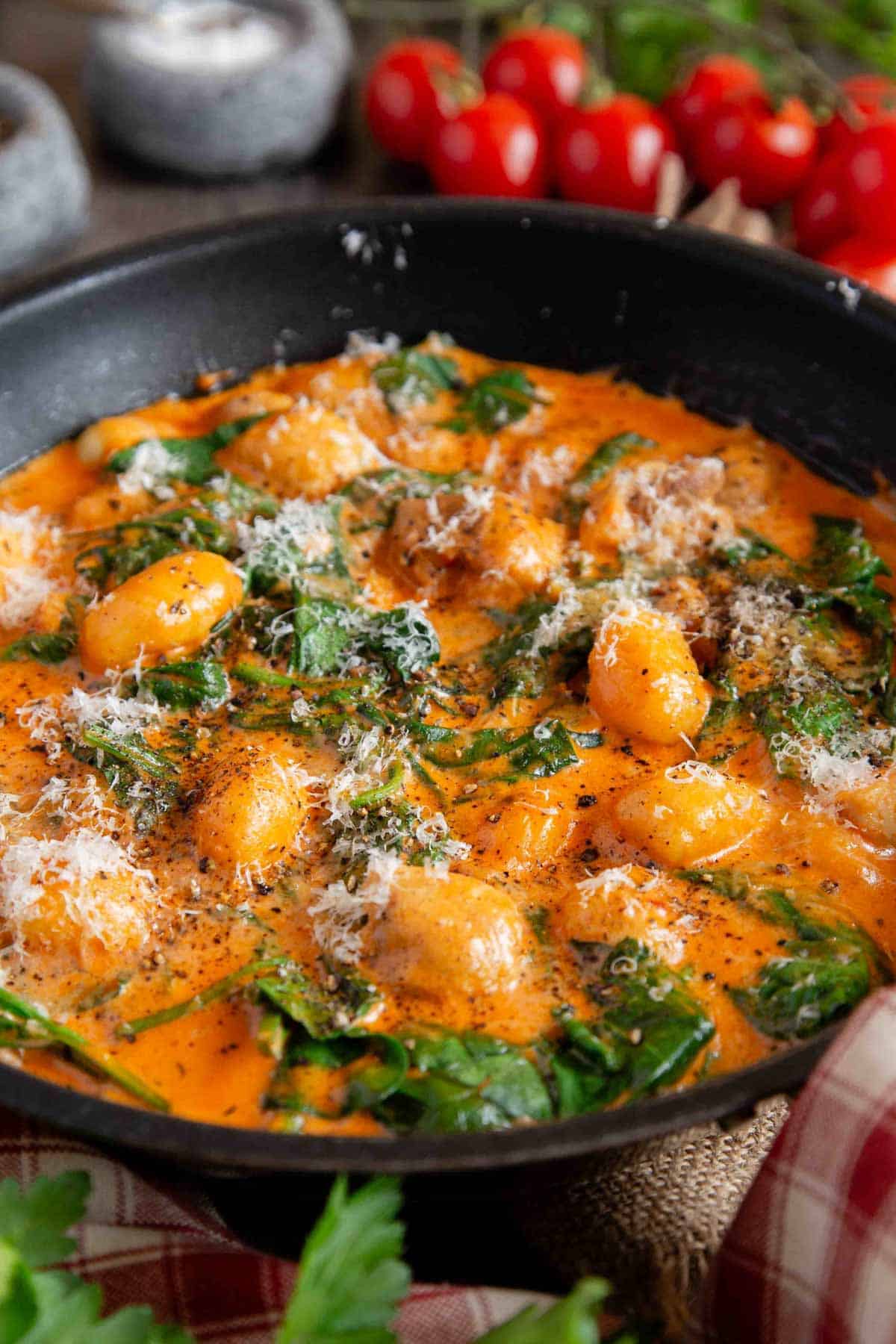Chicken gnocchi in a creamy orange coloured sauce with green wilted spinach in the cooking pan ready to serve