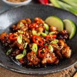 Close up of golden brown honey chilli chicken with garnish in a dark bowl