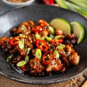 A close up of honey chilli chicken garnished with sesame seeds and chilli and spring onion slices