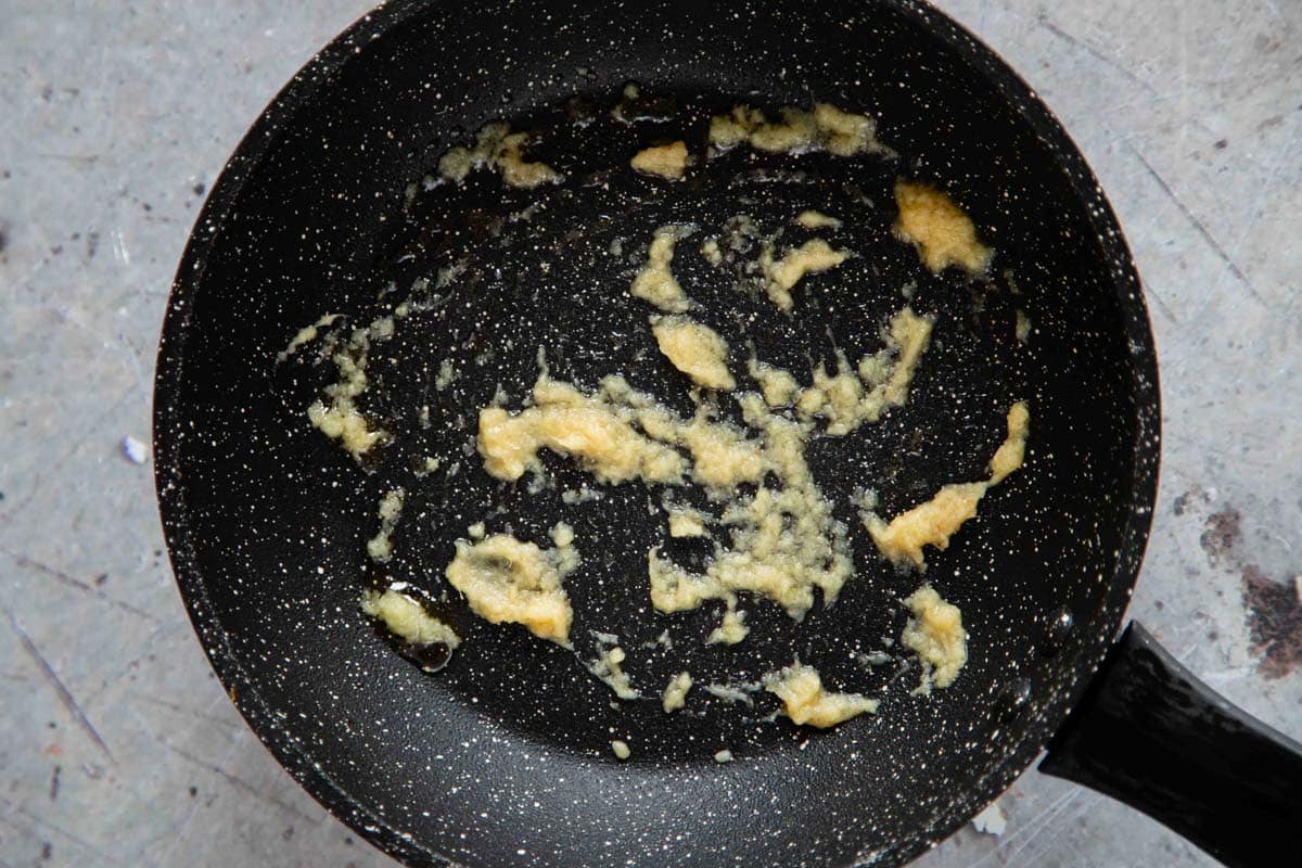 Garlic and ginger paste being cooked in a black frying pan