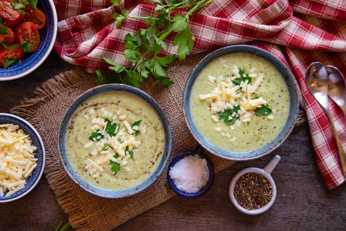 two bowls of soup from above surrounded with pots of salt pepper more cheese and a tomato salad