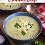 a bowl of soup in close up showing green soup garnished with pale cheddar cheese and parsley leaves