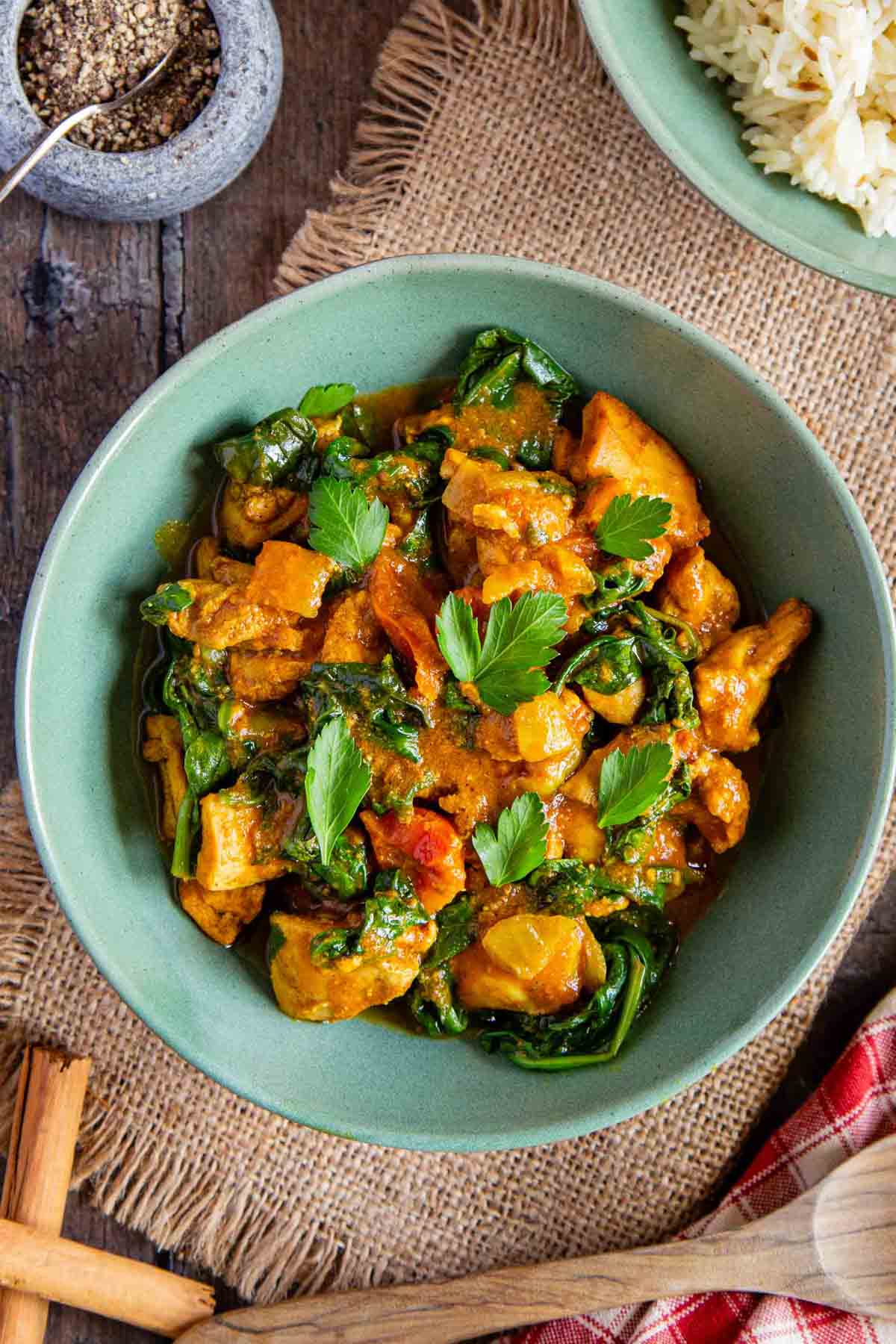 A bowl of orange chicken saag curry garnished with green parsley leaves