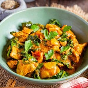 Bright orange chicken saag contrasting with green spinach and parsley garnish