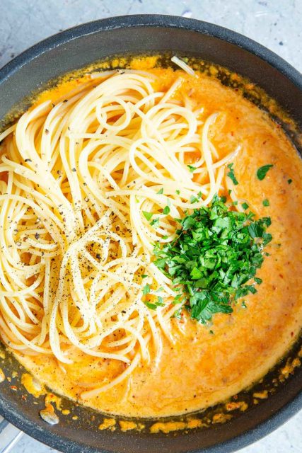 The cooked pasta and chopped herbs are added to the pan of sauce.