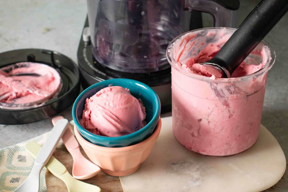 Pale pink raspberry froyo in a small blue bowl next to a larger pot holding more