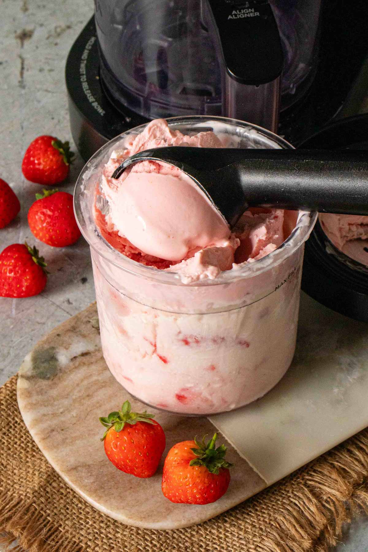 Ninja Creami strawberry frozen yoghurt in the pot with a scoop being taken out and more fruit surrounding