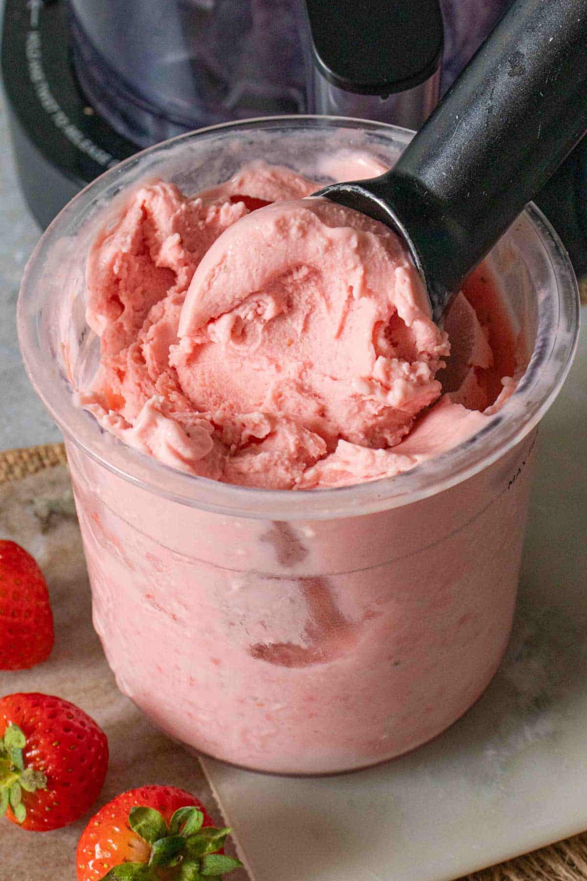 A pot of pale pink strawberry ice cream with a scoop being taken out