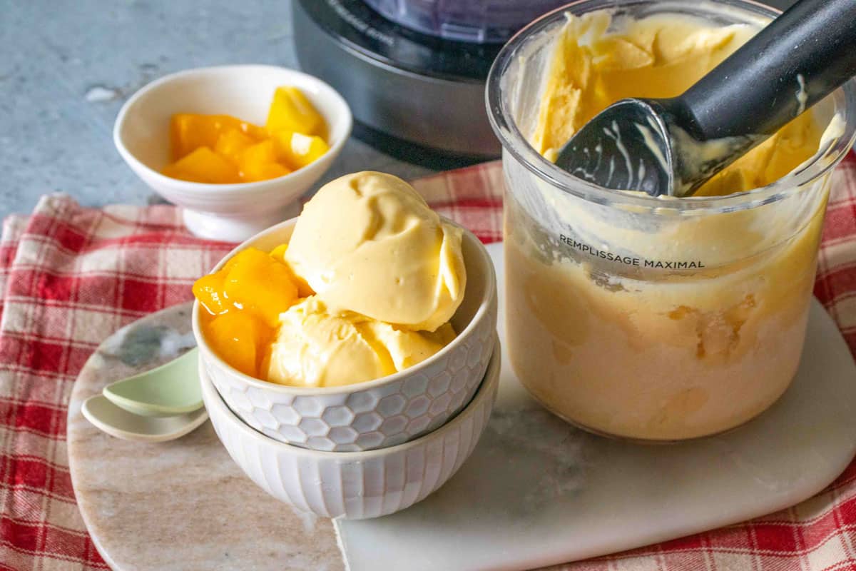 A serving of mango ice cream next to a Ninja Creami pot with ice cream scoop