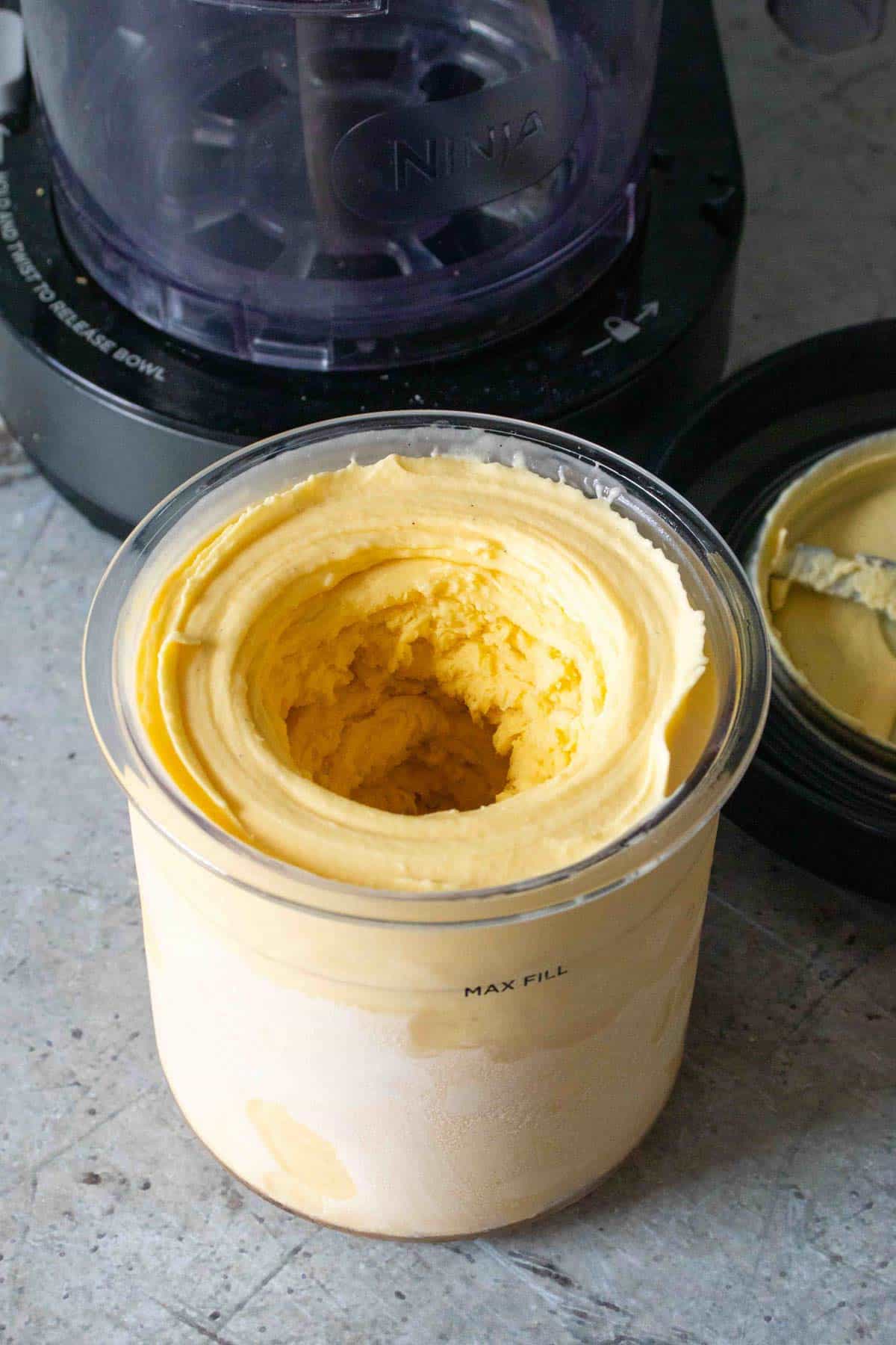 Pale yellow ice cream in the pot after processing showing the hole in the centre from the blades