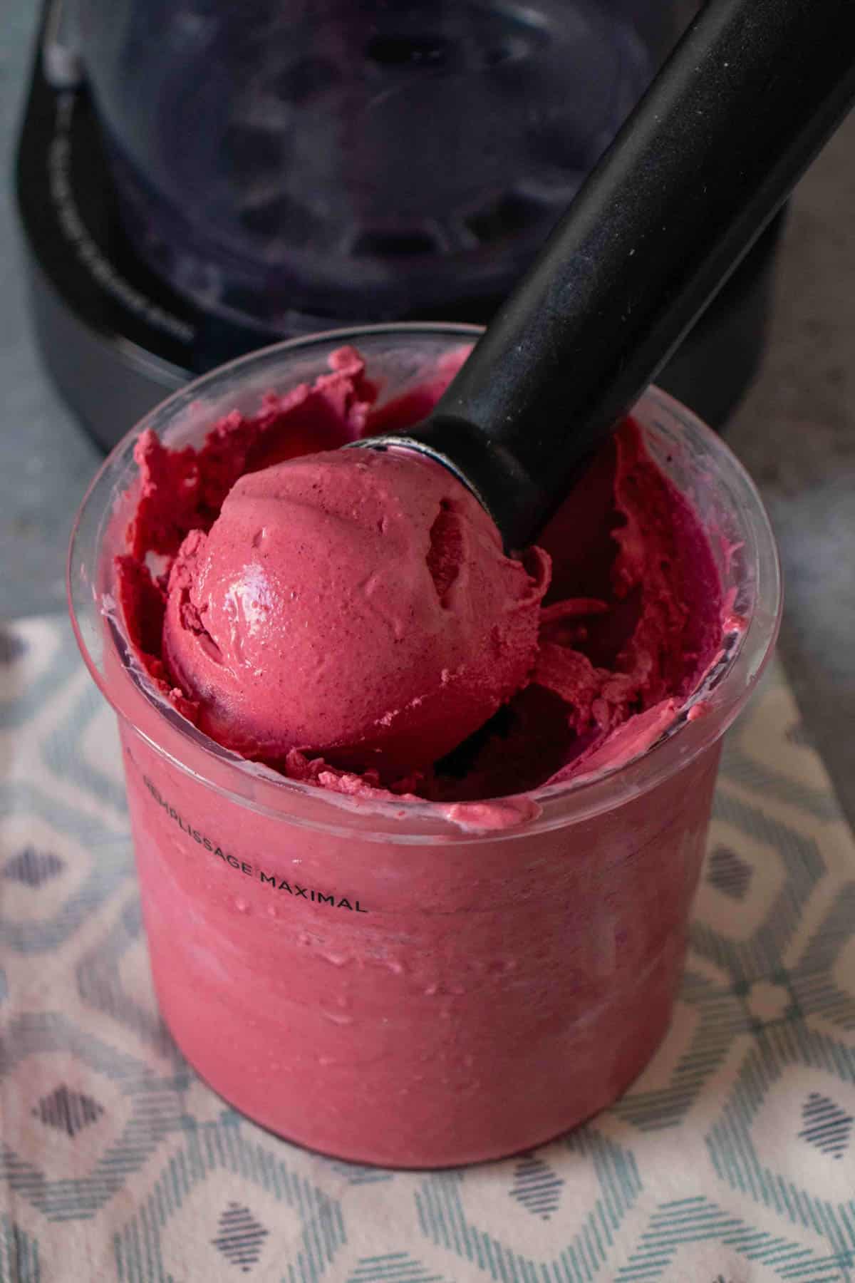 An ice cream scoop filled with pink mixed fruit frozen yoghurt being taken from the Ninja Creami pot
