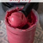 A Ninja Creami pot full of pink mixed berry froyo with a scoop being removed