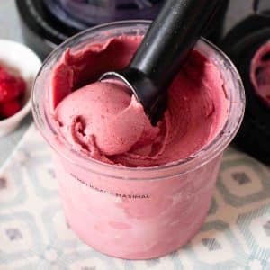 A close up of scooping raspberry ice cream from the full pot